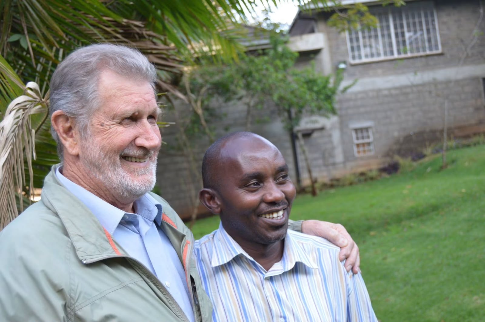 An older founding leader with a gray beard stands beside a colleague in a striped shirt, arm around his shoulder, in the gardens at Thayu resort during the September 2016 SPEC retreat.